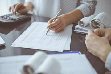 Woman accountant using a calculator and laptop computer while counting taxes for a client. Business...
