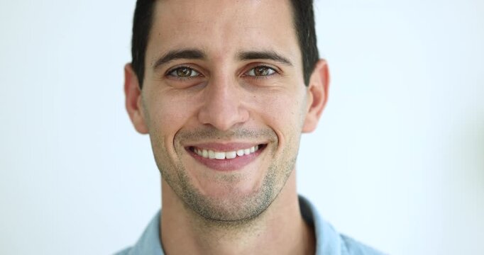 Serious attractive young Hispanic man getting happy, positive, cheerful, looking at camera with toothy smile, laughing. Handsome black haired 20s male Latin model close up cropped facial portrait