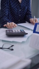 Female accountant is using a laptop computer and calculator for counting taxes at a glass desk in office. Woman in business audit and finance