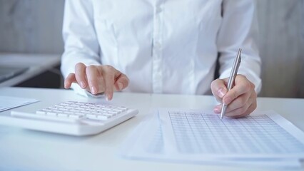 Businesswoman with white blues calculating finance with calculator and taking notes at office table. Audit and taxes