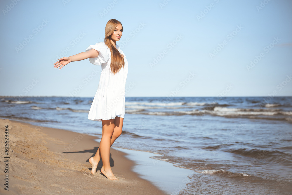 Wall mural Happy smiling beautiful woman is walking on the ocean beach with open arms