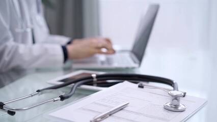 Clipboard with medical records and stethoscope are lying on the glass table while doctor woman is using tablet computer on the glass table. Medicine concept