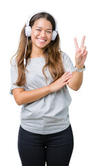 Young beautiful woman wearing headphones listening to music over isolated background smiling with happy face winking at the camera doing victory sign. Number two.