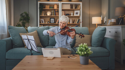 Mature senior caucasian woman learn to play violin practice at home