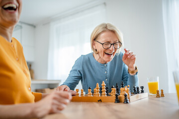 two women mature senior females sisters play chess board game at home