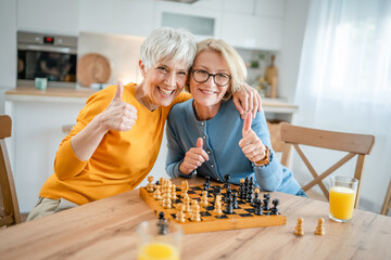 two women mature senior females sisters play chess board game at home