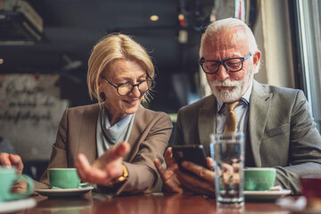 Stylish Senior Business Partners Sharing Digital Insights at Cafe