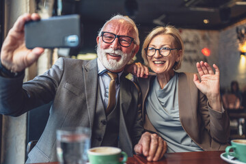Senior couple take selfie photos self portraits or video call at cafe