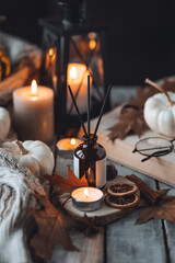 Home comfort, coziness, aromatherapy. Cozy fall interior with knitted wool warm sweater, burning candles and autumn aroma perfume diffuser. Pumpkin pie scent, maple sirup, cinnamon, anise, dry citrus