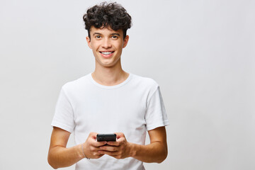 smiling young man with smartphone standing against light background, modern lifestyle concept, casual attire, technology and connection theme, happy expression, youth engagement, innovation