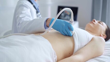 Doctor man, wearing blue medical gloves, is using ultrasound equipment on the breast of a female patient lying down for a medical cardiology examination. Medicine concept © volha_r