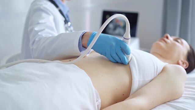 Doctor man, wearing blue medical gloves, is using ultrasound equipment on the breast of a female patient lying down for a medical cardiology examination. Medicine concept