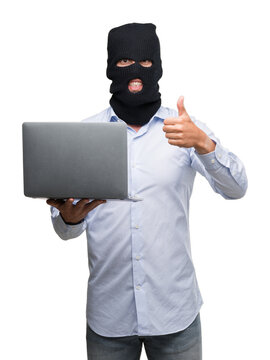 Business hacker man holding a computer laptop happy with big smile doing ok sign, thumb up with fingers, excellent sign