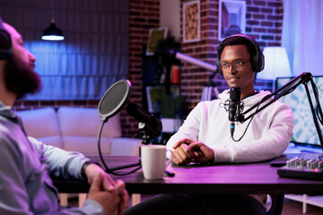 African american influencer recording podcast with guest, using professional equipment in home...