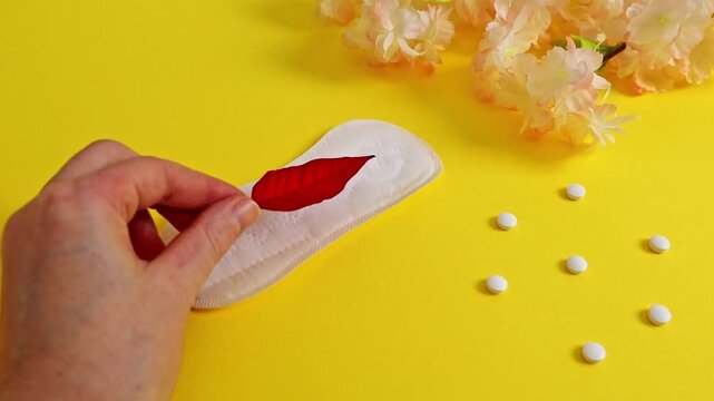 A woman's hand places a red leaf on a panty liner.
