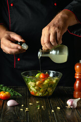 Chef at the kitchen table prepares a vegetable lunch. The cook adds oil to the vegetable salad. Service concept for a restaurant or hotel