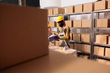 Diverse stockroom employees checking goods inventory report, while preparing customers orders in...