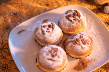 Four Halloween themed sweet buns with spooky faces sprinkled with powdered sugar on white plate, Background with spider web pattern, Halloween dessert concept,