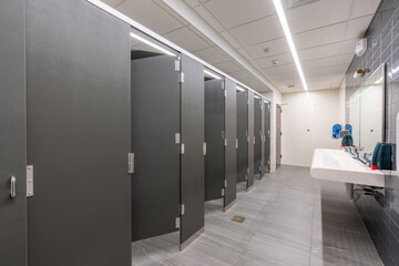 Public restroom with gray and white tile stalls, sink and lavatories