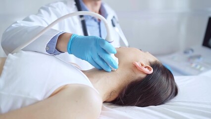 Fototapeta premium Doctor man wearing blue medical gloves is using ultrasound equipment on neck of female patient lying down for a medical examination