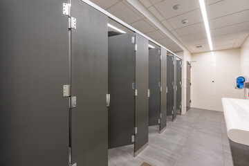 Public restroom with gray and white tile stalls, sink and lavatories