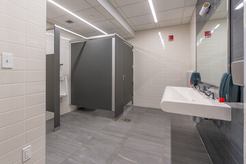Public restroom with gray and white tile stalls, sink and lavatories