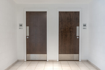 Photo of a pair of dark brown wooden public restroom doors with silver hardware.