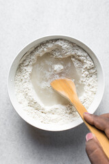 Overhead view of artisan bread dough being mixed in a white mixing bowl, top view of dry bread dough, process of making white bread