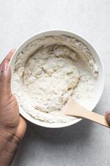 Overhead view of artisan bread dough being mixed in a white mixing bowl, top view of dry bread dough, process of making white bread