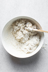 Overhead view of artisan bread dough being mixed in a white mixing bowl, top view of dry bread dough, process of making white bread