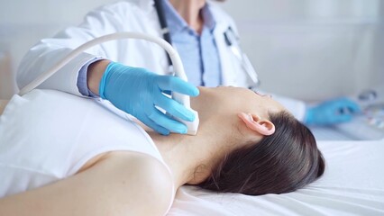 Obraz premium Doctor man wearing blue medical gloves is using ultrasound equipment on neck of female patient lying down for a medical examination