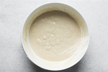 Overhead view of nigerian puff-puff dough being mixed with a wooden spoon, puff-puff dough in a white mixing bowl, process of making puff-puff or bofrot