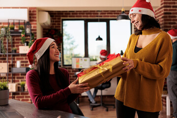 Startup company women employees celebrating christmas holiday and exchanging gifts. Smiling asian and caucasian colleagues sharing presents in winter decorated office at xmas eve