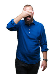 Young caucasian hipster man wearing glasses over isolated background smiling and laughing with hand on face covering eyes for surprise. Blind concept.