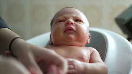 Newborn baby during bath time, looking around with a thoughtful expression, moment of curiosity and awareness, reflecting the nurturing care provided by the mother