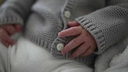 Newborn baby gently grasping sweater button, showcasing tiny fingers and delicate skin texture, close-up of baby's hand and button, tender moment captured in detail, cozy infant attire