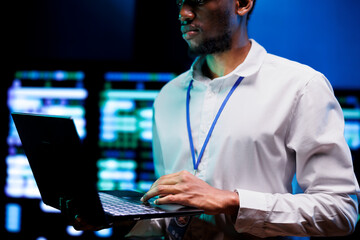 Fototapeta premium Manager using laptop to survey high tech supercomputers providing vast computing resources and storage. Server farm enabling artificial intelligence to process massive datasets for training