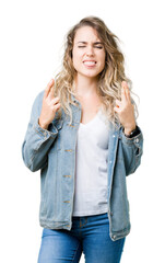 Beautiful young blonde woman wearing denim jacket over isolated background smiling crossing fingers with hope and eyes closed. Luck and superstitious concept.