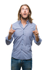 Obraz premium Young handsome man with long hair over isolated background amazed and surprised looking up and pointing with fingers and raised arms.