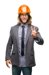 Young handsome architec man with long hair wearing safety helmet over isolated background smiling looking to the camera showing fingers doing victory sign. Number two.