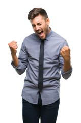 Fototapeta premium Young handsome business man over isolated background very happy and excited doing winner gesture with arms raised, smiling and screaming for success. Celebration concept.