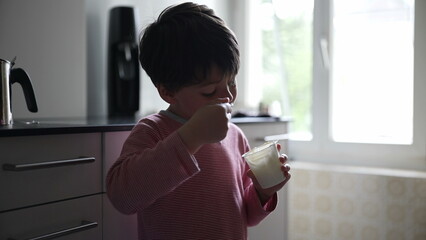 Young boy enjoying a snack in a modern kitchen, with natural light illuminating the scene,...