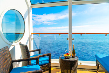 A balcony on a cruise ship at sea with chairs, table, bowl of fruit and champagne bottle with...