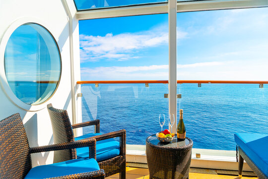 A balcony on a cruise ship at sea with chairs, table, bowl of fruit and champagne bottle with glasses on a sunny day with blue skies.