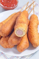 Heap of corn dogs on white plate, served with ketchup, vertical closeup