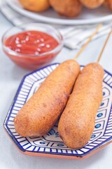 Two corn dogs on white blue plate, served with ketchup, vertical