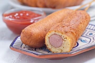 Corn dogs on white blue plate, served with ketchup, horizontal closeup