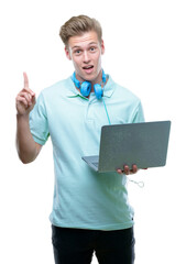 Young handsome blond man using a laptop surprised with an idea or question pointing finger with happy face, number one