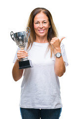 Middle age hispanic winner woman celebrating award holding trophy over isolated background pointing and showing with thumb up to the side with happy face smiling