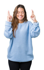 Young beautiful brunette woman wearing blue winter sweater over isolated background smiling crossing fingers with hope and eyes closed. Luck and superstitious concept.